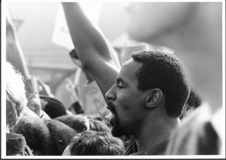 Close-up of an African-American man standing in a crowd with his arm raised in the air. 