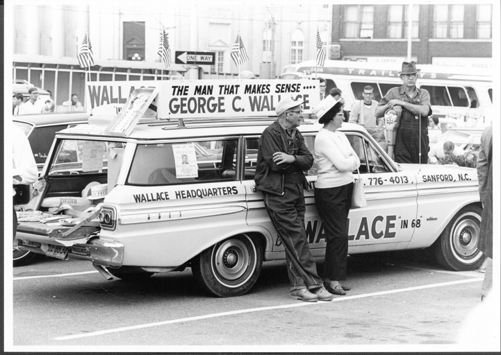 A man and woman standing in front of a George Wallace campaign car. 