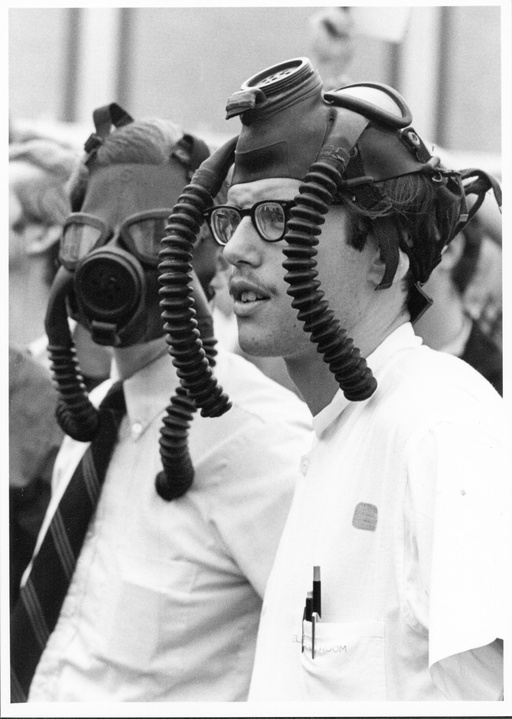 Two men with gas masks, one covering his face and the other on top of his head. 
