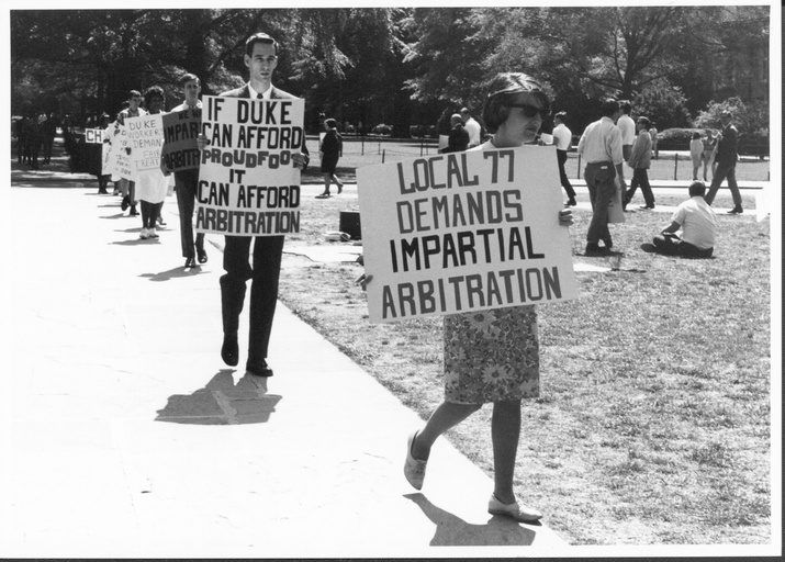 A line of protesters carrying signs on Duke's campus. 