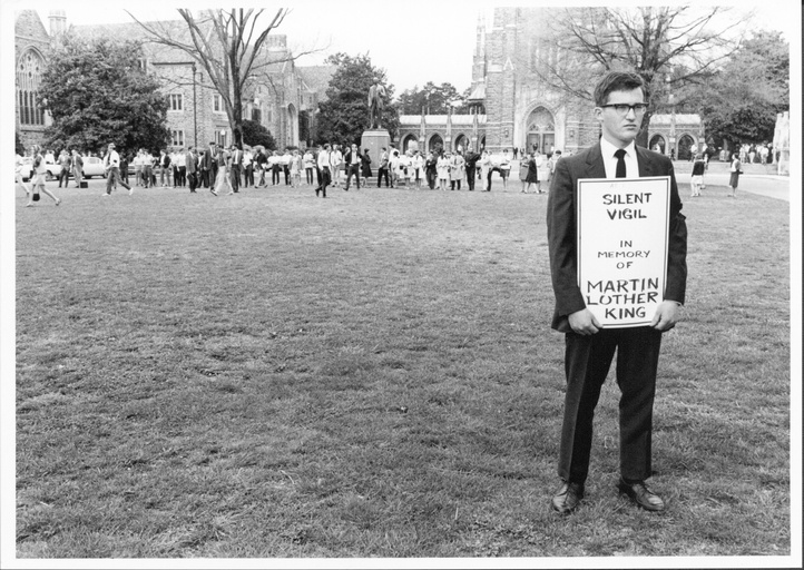 A large crowd gathered on Duke's campus. In the foreground one white man stands with a sign that says "Silent Vigil in Memory of Martin Luther King."