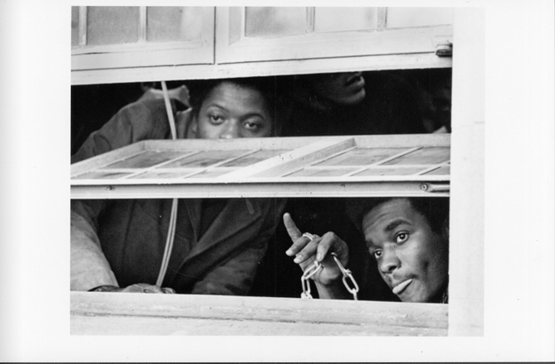Two African-American people inside a building peer through a window. 
