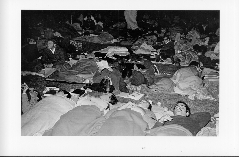 A large crowd of people laying on the ground with blankets and sleeping bags. 