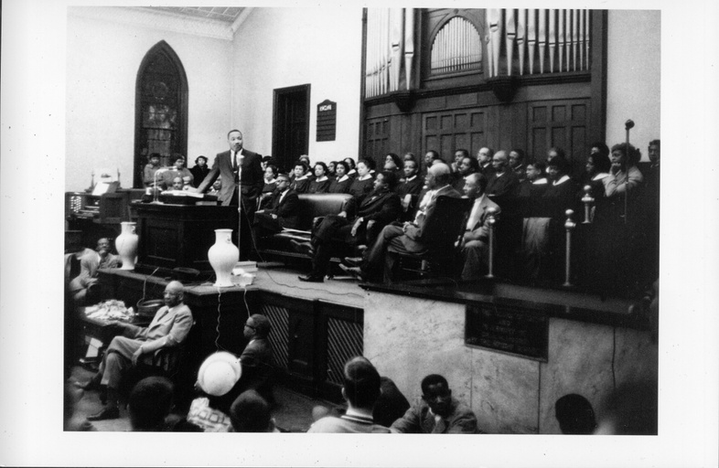 Dr. Martin Luther King preaching in a church. The organ and choir are visible behind him. 
