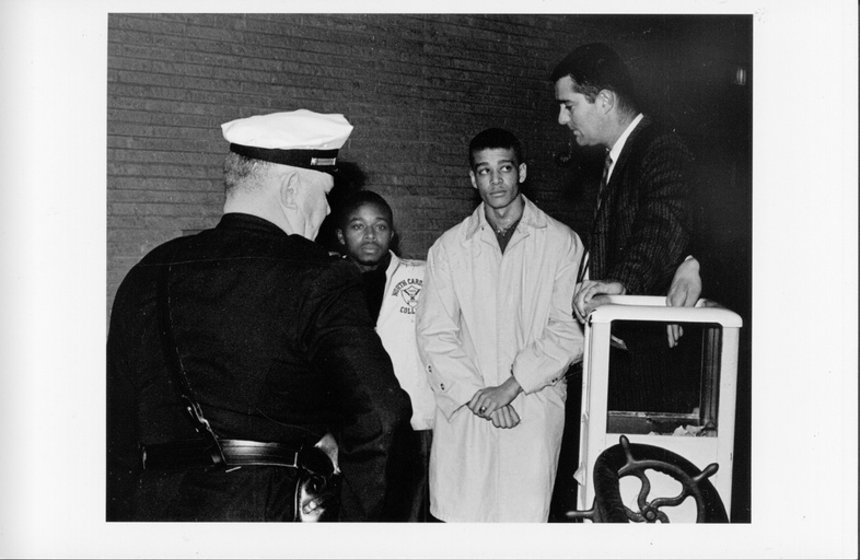 Two black men, a white man, and a white police officer stand near each other. 
