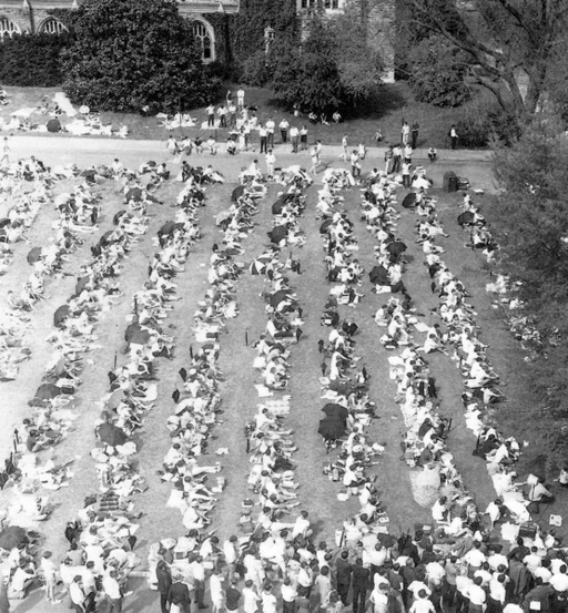 A large crowd of people sit on a lawn near Duke Chapel. 